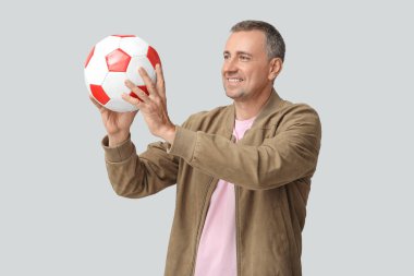 Gri arka planda futbol topuyla oynayan yakışıklı olgun bir adam.