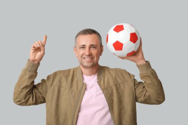 Futbol topuyla yakışıklı, olgun bir adam gri arka plandaki bir şeyi işaret ediyor.