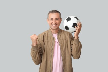 Gri arka planda futbol topu olan mutlu ve olgun bir adam.