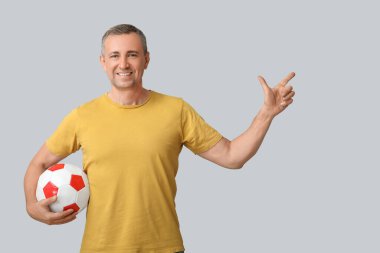 Futbol topuyla yakışıklı, olgun bir adam gri arka plandaki bir şeyi işaret ediyor.