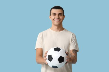 Mavi arka planda futbol topu olan yakışıklı genç adam.