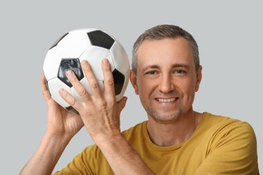 Gri arka planda futbol topuyla oynayan yakışıklı olgun bir adam.