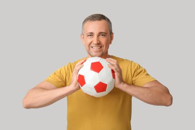 Gri arka planda futbol topu olan yakışıklı olgun bir adam.