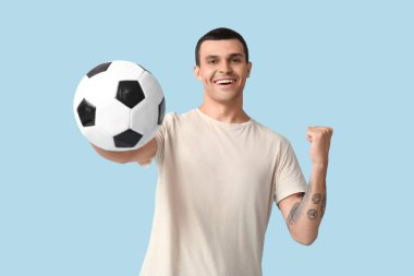 Mavi arka planda futbol topu olan yakışıklı genç adam.