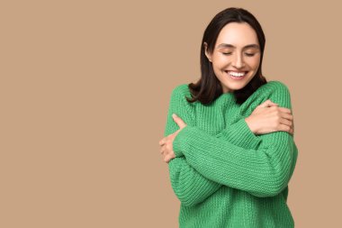 Kahverengi arka planda kendine sarılan genç bir kadın.