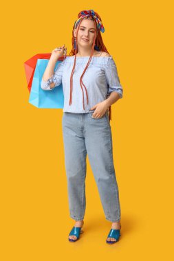 Sarı arka planda rastalı ve alışveriş çantalı güzel bir genç kadının portresi.