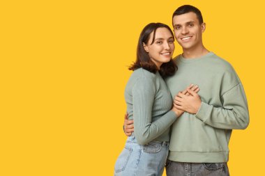 Sarı arka planda kucaklaşan neşeli genç çift
