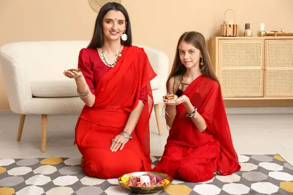 stock image Beautiful mother with her daughter holding candles, flowers and diya lamps at home. Divaly celebration