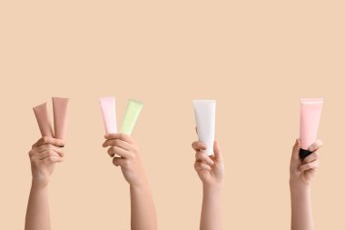 Bej arka planda farklı kozmetik kremlerden tüpler olan kadın elleri