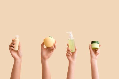 Bej arka planda farklı kozmetik ürünleri olan kadın elleri