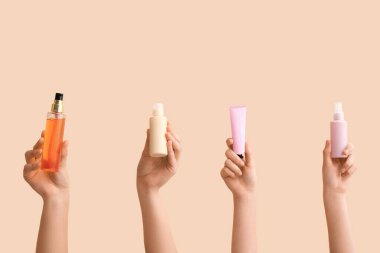 Bej arka planda farklı kozmetik ürünleri olan kadın elleri