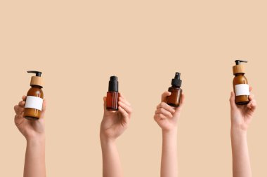 Bej arka planda farklı kozmetik ürünleri olan kadın elleri