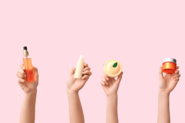 Pembe arka planda farklı kozmetik ürünleri olan kadın elleri