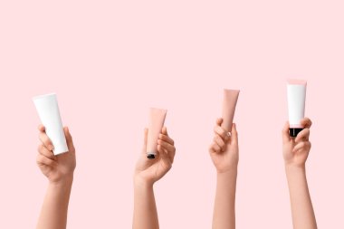 Pembe arka planda farklı kozmetik krem tüpleri olan kadın elleri