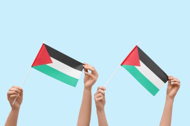 Mavi arka planda Filistin bayrakları olan kadın eller