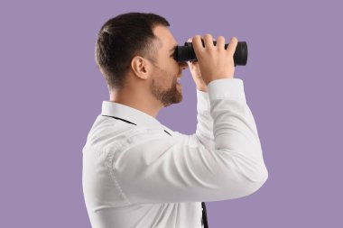 Dürbünle leylak arkaplanına bakan genç bir iş adamı.