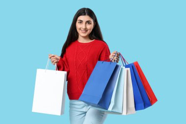 Mavi arka planda alışveriş torbaları olan mutlu, genç bir kadın.