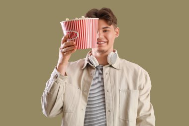 Yeşil arka planda patlamış mısırla kovayı tutan yakışıklı genç adam.