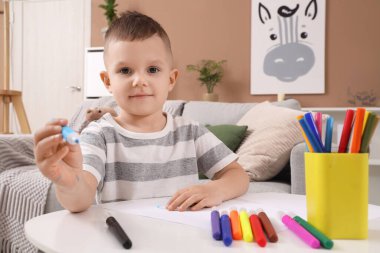 Evdeki masada keçeli kalemlerle resim çizen sevimli küçük çocuk.