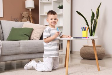 Evdeki masada keçeli kalemlerle resim çizen sevimli küçük çocuk.