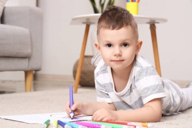 Evde keçeli kalemle çizen küçük çocuk.