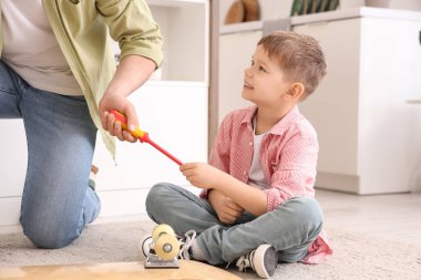 Young man and his little son fixing skateboard at home