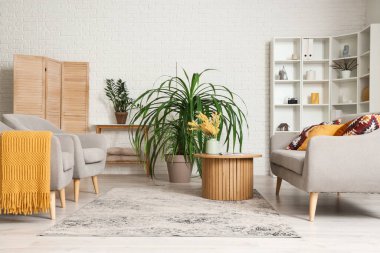 Konforlu kanepe, çiçekli kahve masası ve oturma odasında çiçek.