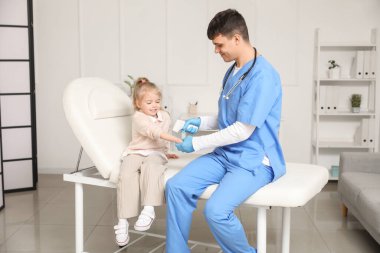 Male pediatrician measuring temperature of little girl with infrared thermometer in clinic