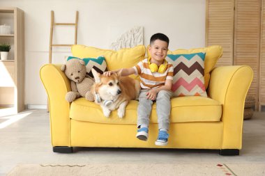 Kulaklıklı şirin Corgi köpeği olan mutlu Asyalı çocuk evdeki kanepede oturuyor.