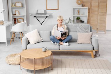 Evdeki kanepede kısa saç dergisi okuyan genç bir kadın.