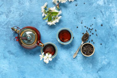 Fincanlı çaydanlık, bir kaşık kuru yeşil çay ve mavi grunge arka planda çiçekler.