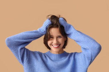 Kahverengi arka planda zarif mavi süveter giyen mutlu genç kadın.