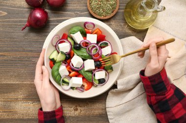 Sağlıklı sebze salatası ve ahşap arka planda malzemelerle dolu kadın elleri.