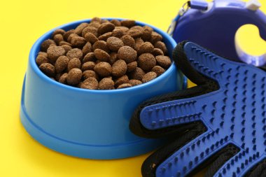 Kuru hayvan maması, tasma ve fırçalama eldiveni sarı arka planda, yakın plan.