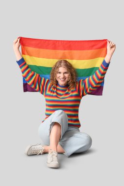 Gri arka planda oturan LGBT bayrağıyla güzel genç bir kadın.