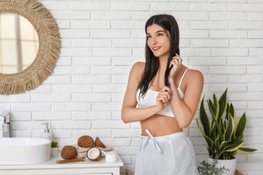 Güzel genç bir kadın banyodaki saçlara hindistan cevizi yağı sürüyor.