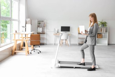 Ofiste koşu bandında dizüstü bilgisayar eğitimi alan genç bir iş kadını.