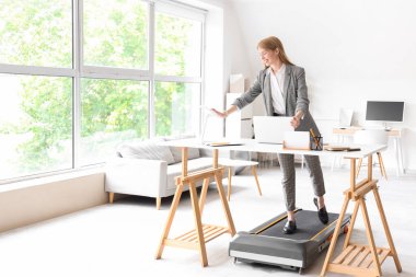 Ofisteki koşu bandında tablet bilgisayarla çalışan genç iş kadını.