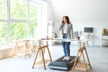 Ofisteki koşu bandında cep telefonuyla konuşan güzel bir iş kadını.