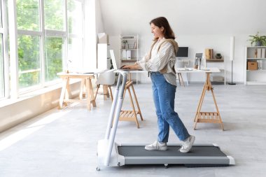 Ofiste koşu bandında dizüstü bilgisayar eğitimi almış güzel bir iş kadını.