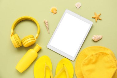 Yeşil arka planda kulaklıklı tablet ve plaj aksesuarları. Üst görünüm