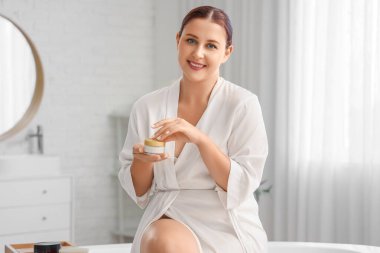 Banyoda krema kavanozu olan güzel ve iri yarı bir kadın.