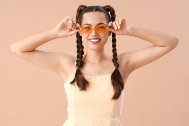 Güneş gözlüklü, bej arka planda örgüleri olan güzel, genç, mutlu, şık bir kadın.