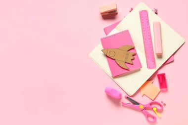 Pembe arka planda farklı okul kırtasiyesine sahip karton roket.