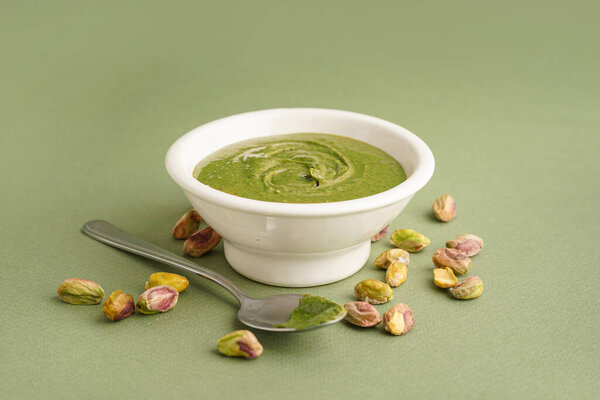 Чаша с вкусной фисташковой пастой и ложкой на зеленом фоне