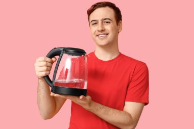 Pembe arka planda modern elektrikli su ısıtıcısı olan yakışıklı genç adam.