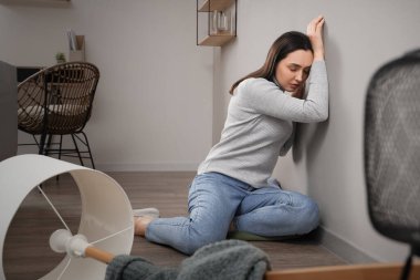 Dağınık odada duvarın yanında oturan depresif genç kadın.