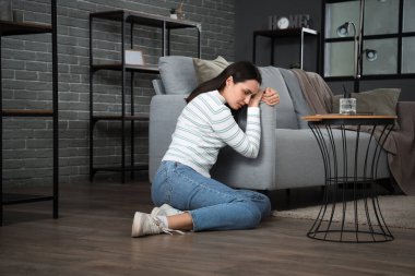 Evdeki kanepenin yanında oturan depresyondaki genç kadın.