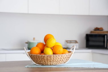 Beyaz mutfaktaki sepetin üzerinde turunçgiller var.