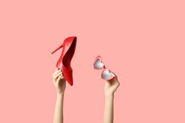 Güneş gözlüklü kadın elleri ve pembe arka planda topuklu ayakkabılar.